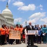 Photo of Rep. Thompson speaking at a podium in front of a crowd of advocates. The Capitol building is in the background.